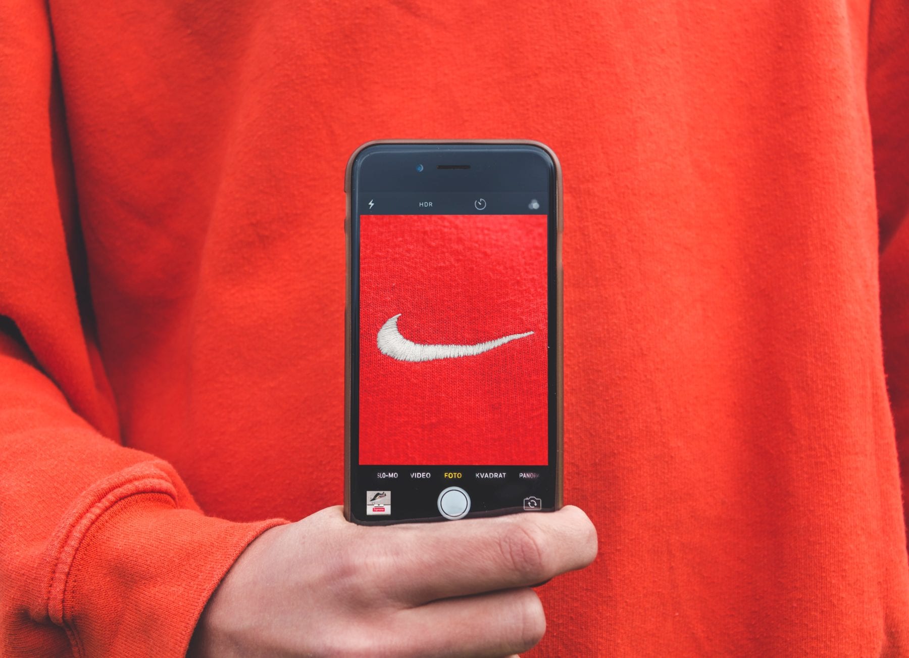A photograph of someone taking a cell phone photo of the nike swoosh against a red background.